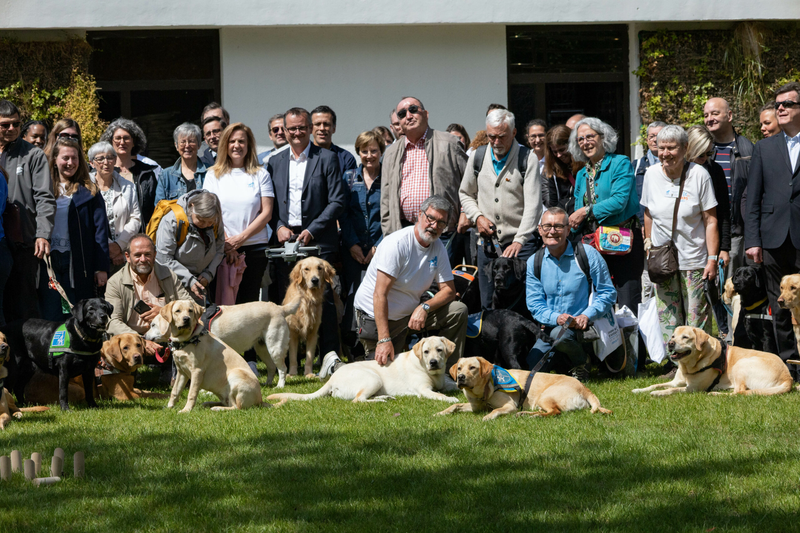 Les invités et salariés posent tous ensemble avec les chiens guides à l'extérieur lors de la célébration des 50 ans de l'association à Vincennes